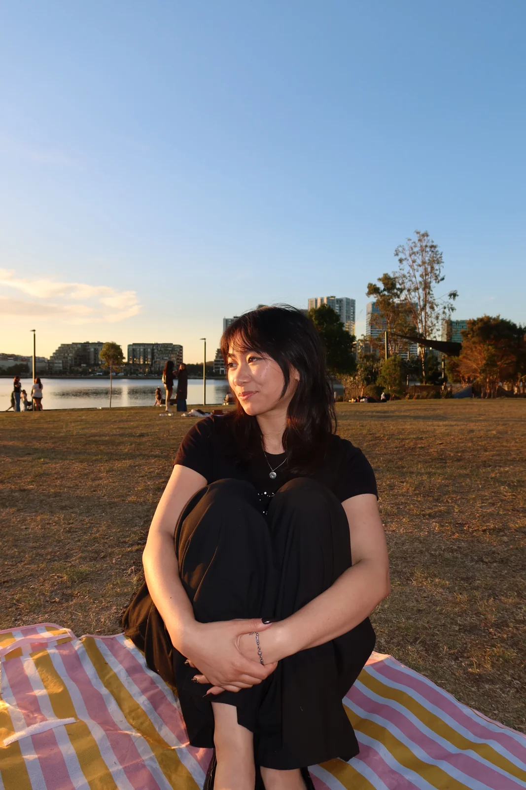 Natasha sitting on a picnic blanket by the water at sunset